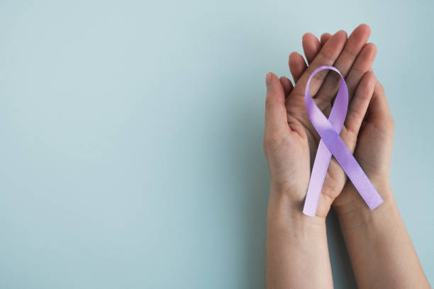 Womans hands hold lavender color awareness ribbon on a light background.  
